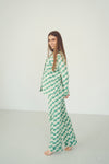 A woman modeling a two-piece pajama set with a green and white checkerboard pattern, standing barefoot against a plain white studio background.