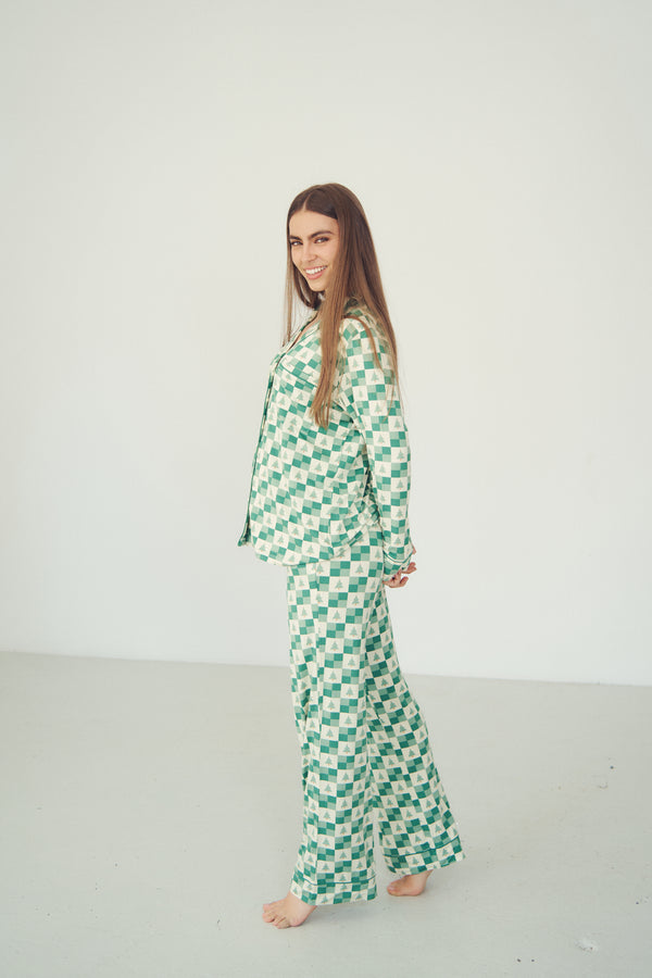 A woman modeling a two-piece pajama set with a green and white checkerboard pattern, standing barefoot against a plain white studio background.