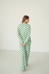 A woman wearing a green and white checkered long-sleeve top and matching wide-leg pants, shown from the back in a minimalist studio setting.
