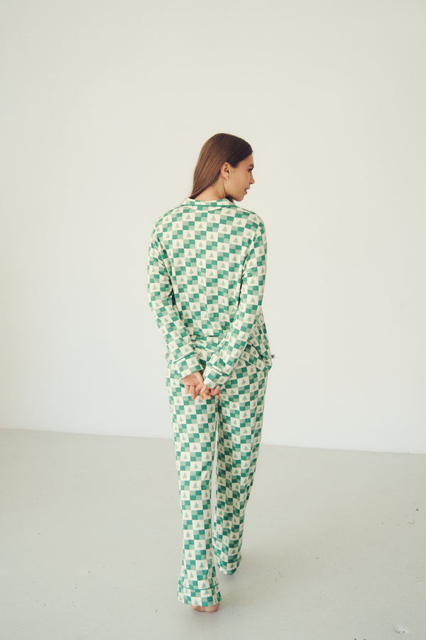 A woman wearing a green and white checkered long-sleeve top and matching wide-leg pants, shown from the back in a minimalist studio setting.