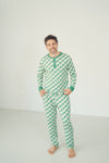 A man wearing a green and white checkered long-sleeve pajama set with a green Henley collar, standing barefoot against a plain white studio background.