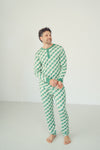 A man wearing a green and white checkered long-sleeve pajama set with a green Henley neck and cuffs, standing barefoot against a plain white studio background.