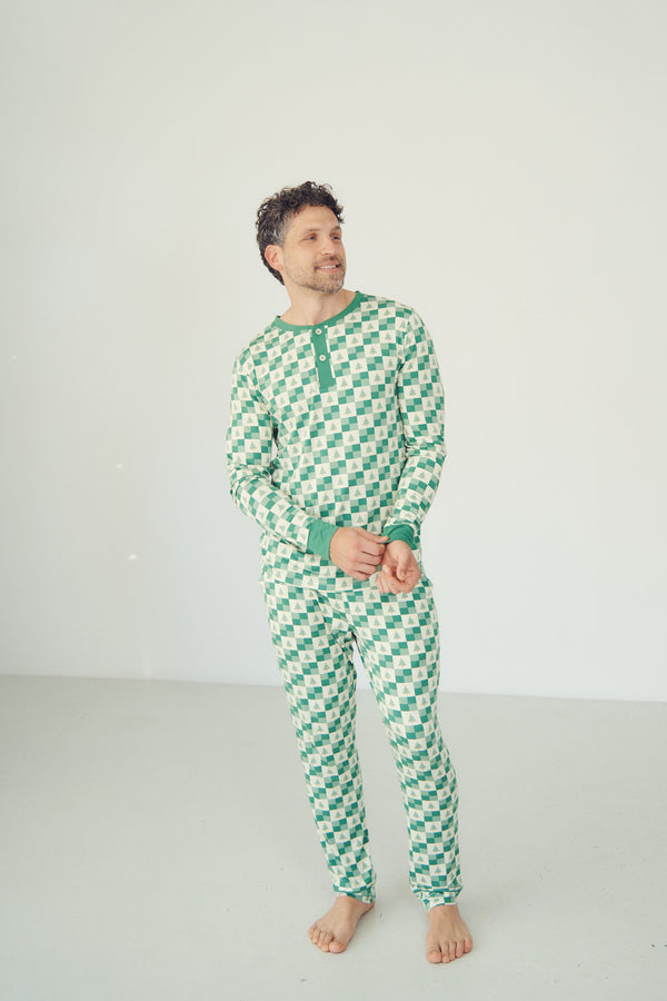 A man wearing a green and white checkered long-sleeve pajama set with a green Henley neck and cuffs, standing barefoot against a plain white studio background.