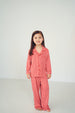 A young girl with long dark hair stands barefoot against a plain white studio background, wearing a matching red and white striped pajama set with a long-sleeve top and pants.