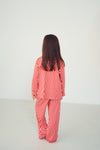A woman viewed from behind wearing a red and white checkered long-sleeve pajama set in a minimalist white studio.