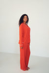 A woman modeling a bright orange-red two-piece pajama set with white piping details, standing against a plain white studio background.