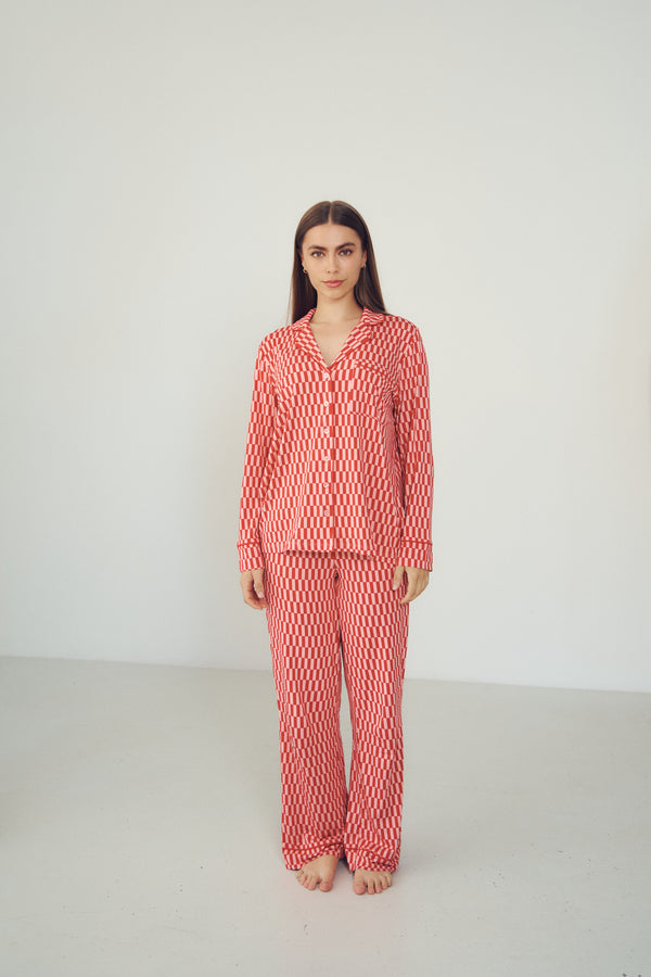 A woman stands barefoot in a studio wearing a matching long-sleeve pajama set with a red and white wavy geometric pattern.
