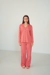 A woman stands barefoot in a studio wearing a matching long-sleeve pajama set with a red and white wavy pattern.