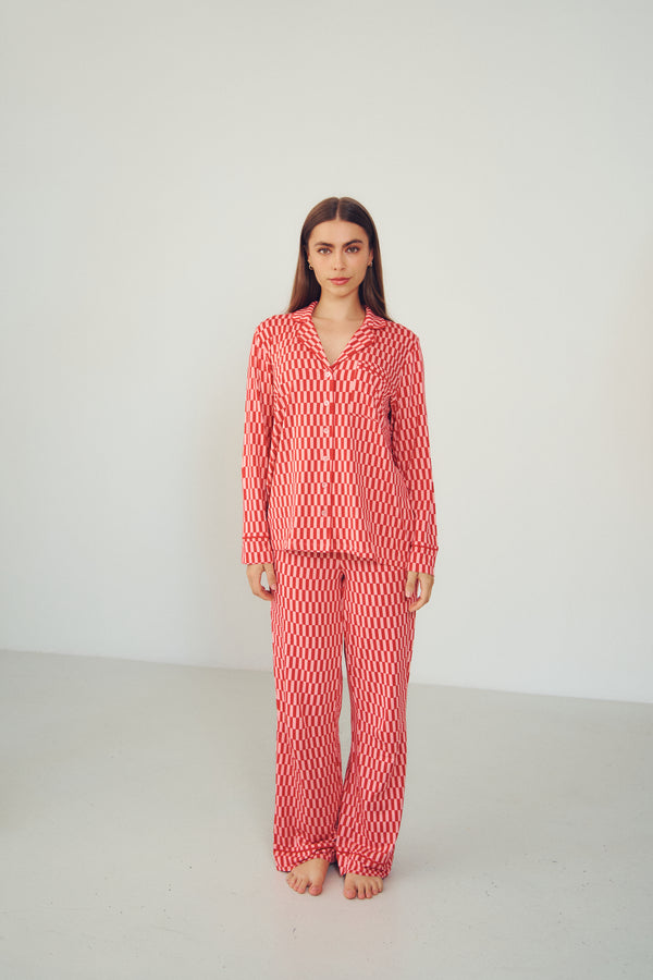 A woman stands barefoot in a studio wearing a matching long-sleeve pajama set with a red and white wavy pattern.
