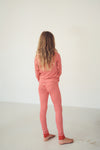 A child standing with their back to the camera, wearing a matching red and white patterned long-sleeve top and pants set in a minimalist studio setting.