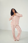 A woman modeling a two-piece plaid pajama set with a white base and red grid pattern, standing against a plain light gray studio background.