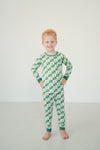 A young boy with red hair stands barefoot in a studio setting, wearing a long-sleeve one-piece pajama set with a green and cream checkerboard pattern.