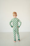 A child standing with hands on hips, viewed from behind, wearing a green and cream checkerboard patterned long-sleeve pajama set in a minimalist studio setting.