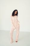 A woman modeling a matching long-sleeve pajama set with an abstract pink and white pattern, standing against a plain white studio background.