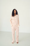 A woman stands barefoot in a studio wearing a matching long-sleeve pajama set with a white base and a pink abstract floral pattern.