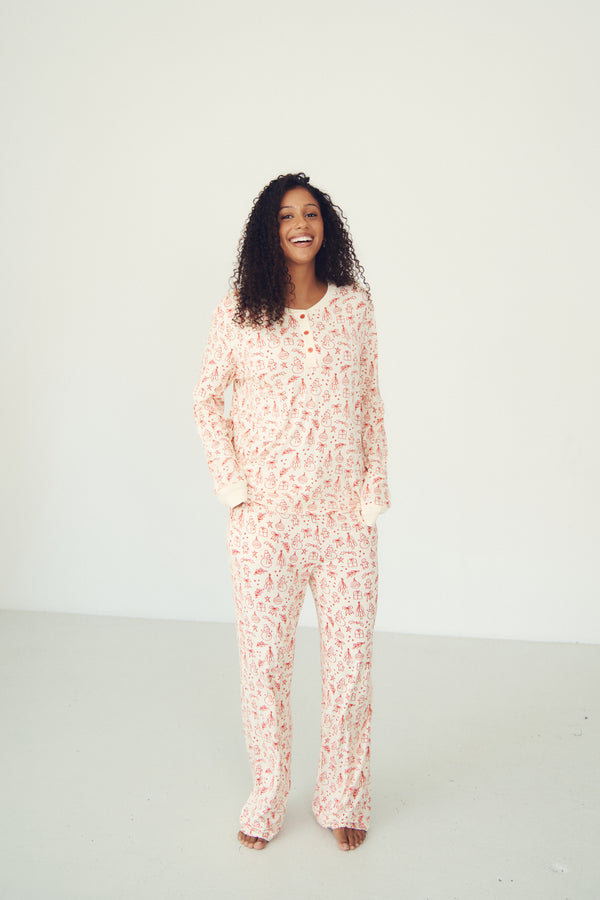 A woman stands barefoot in a studio wearing a matching long-sleeve pajama set with a white base and a pink abstract floral pattern.