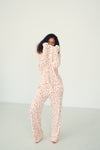 A woman modeling a matching two-piece lounge set consisting of a long-sleeve top and pants, featuring a light pink and white abstract pattern, set against a plain white studio background.