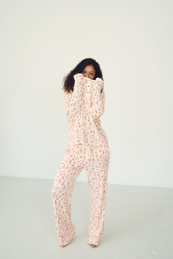 A woman modeling a matching two-piece lounge set consisting of a long-sleeve top and pants, featuring a light pink and white abstract pattern, set against a plain white studio background.