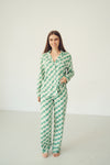 A woman modeling a two-piece pajama set with a green and white checkerboard pattern, standing against a plain off-white studio background.