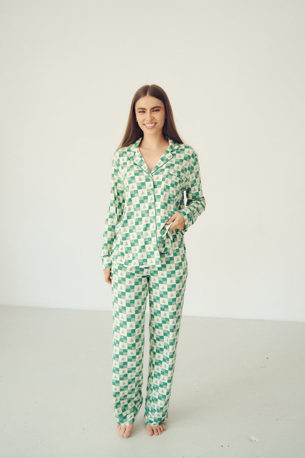 A woman modeling a two-piece pajama set with a green and white checkerboard pattern, standing against a plain off-white studio background.