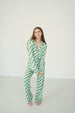 A woman modeling a matching green and white checkered pajama set, consisting of a long-sleeve button-up top and matching pants, standing against a plain white studio background.