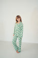 A young girl stands barefoot in a bright white studio setting, wearing a green and white checkered long-sleeve pajama set.