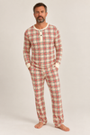 A man modeling a two-piece long-sleeve pajama set with a red, green, and cream plaid pattern, standing against a light gray studio background.