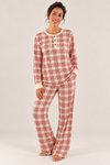 A woman modeling a matching long-sleeve pajama set with a re and white tartan pattern, standing against a plain white studio background.