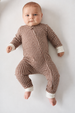 A baby lying on their back wearing a brown and white checkered long-sleeve footless sleeper with white cuffs, photographed against a plain white background.