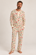 A man wearing a holiday/winter patterned long-sleeve pajama top and matching pants, standing barefoot against a plain light gray studio background.