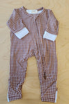 A baby long-sleeve footless one-piece pajama with a brown and white checkered pattern and white cuffs, laid flat on a light wood background.