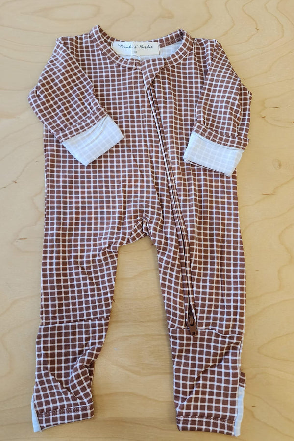 A baby long-sleeve footless one-piece pajama with a brown and white checkered pattern and white cuffs, laid flat on a light wood background.
